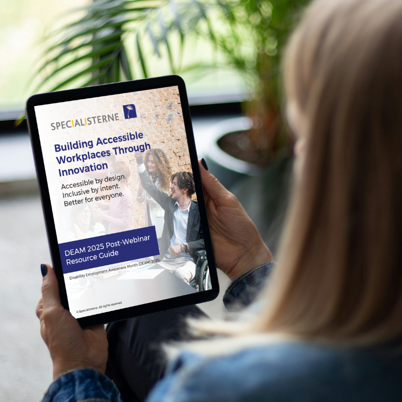 A person holds a tablet displaying the cover of the “Building Accessible Workplaces Through Innovation” DEAM 2025 Post-Webinar Resource Guide from Specialisterne. The cover features the Specialisterne logo and tagline “Accessible by design. Inclusive by intent. Better for everyone.” along with an image of three colleagues smiling and collaborating, including one person using a wheelchair. The scene conveys accessibility, inclusion, and innovation in the workplace.